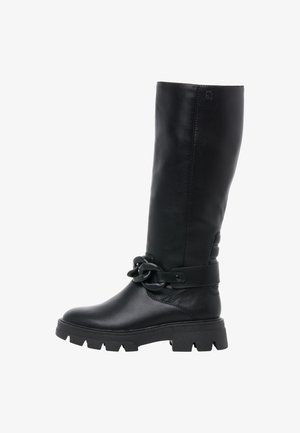 Schwarzer, hoher Lederstiefel mit massiver Sohle und großer dekorativer Kette um den Knöchel, seitlich betrachtet.