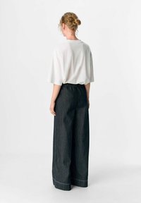 Weiße Kurzarm-T-Shirt kombiniert mit schwarz-weißen gestreiften weit geschnittenen Hosen, die einen elastischen Bund und einen leichten Aufschlag am Saum haben.