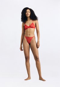 Ensemble bralette et string en dentelle rouge avec des bretelles fines et un motif floral. Le tissu a une texture légère, créant des accents délicats.