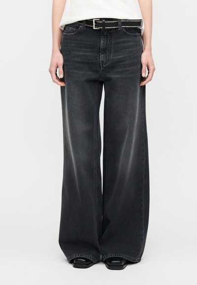 Jean noir à jambes larges en denim délavé, avec une taille haute, un design à cinq poches et une ceinture noire cloutée pour un détail accentué.
