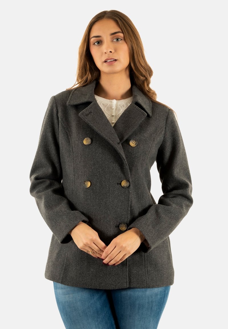 Cappotto grigio in lana doppiopetto con colletto a punte, caratterizzato da due file di bottoni circolari e tasche frontali. Indossato sopra un top leggero.