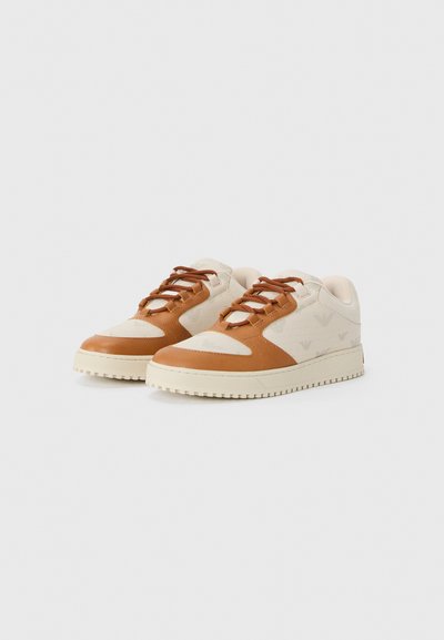 Beige sneakers med brune læderdetaljer, rund tå, snørebåndsdesign, tekstureret overdel og rillet gummisål. Subtile logo mønstre på stoffet.