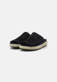 Scarpe slip-on in suede nero con punta arrotondata, dettagli cuciti e una suola spessa di colore crema. Parte superiore testurizzata con un design aperto.