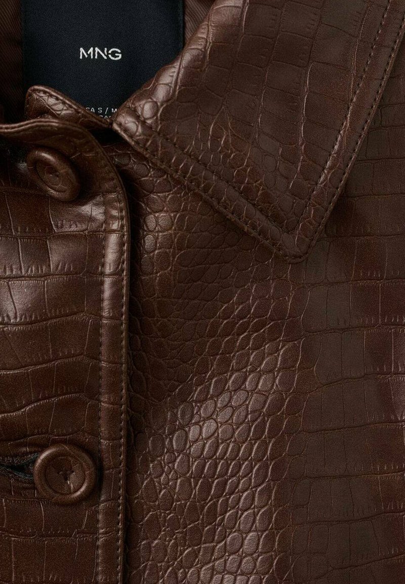 Primer plano del cuello de una chaqueta de cuero marrón con estampado de cocodrilo falso y solapa abotonada con la etiqueta visible de la marca MNG en el interior.
