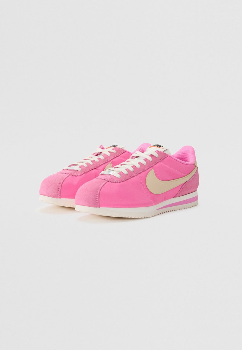 Rosa Wildleder-Sneaker mit einem beigen Swoosh, weißen Schnürsenkeln und einer strukturierten Sohle. Verfügt über eine abgerundete Zehenpartie und einen gepolsterten Schaft.
