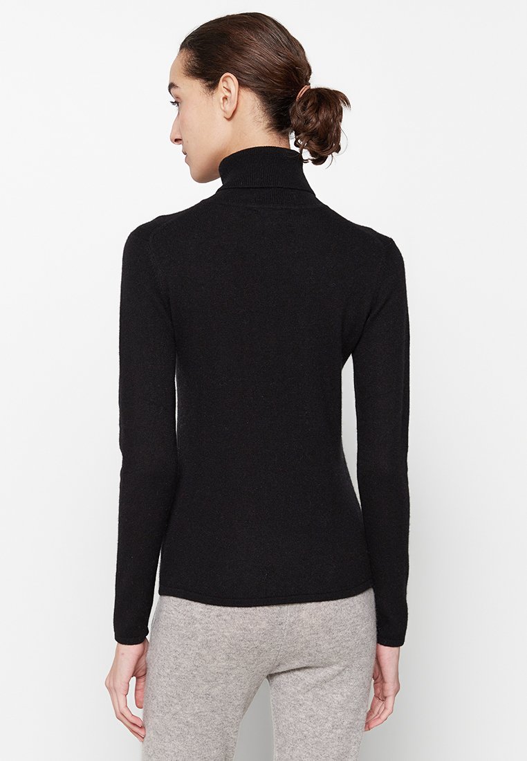 Zwarte coltrui met lange mouwen, aansluitend ontwerp, zachte textuur en subtiele ribbels langs de kraag en manchetten.