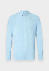 Chemise bleu clair à manches longues avec col et petit logo rectangulaire sur le côté gauche de la poitrine.