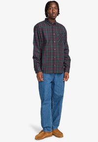 Geruite flanellen overhemd in donk paars en groen, met een button-down kraag, lange mouwen en een borstzak. Draagt een blauwe spijkerbroek en tan schoenen.