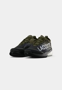 Lacoste atletske cipele s crnom i maslinasto zelenom kombinacijom boja, teksturiranim gornjim materijalom, zaobljenim dizajnom i istaknutim bijelim logotipom.