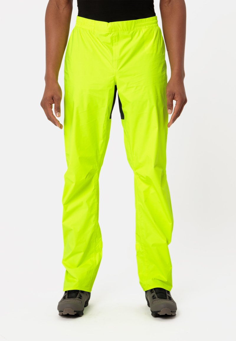 Person wearing bright yellow waterproof pants and black shoes, standing against a plain white background.