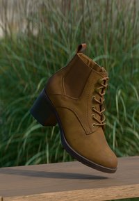Brown ankle boot made of textured material, featuring round toe, lace-up front, and a low stacked heel. Smooth surface with stitching details.