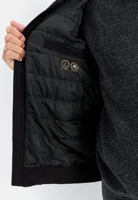 Black jacket interior with quilted lining, featuring water-repellent and stain-resistant icons. Soft fabric with elastic cuffs and hem.