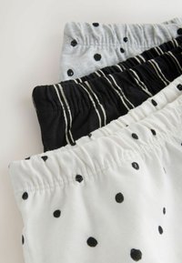 Trzy pary damskich szortów z elastycznymi pasami: białe w czarne kropki, szare w czarne kropki oraz czarne w białe paski.