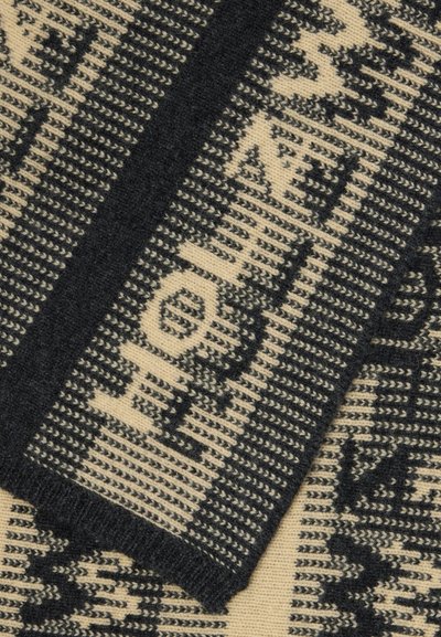 Virkat halsduk i kräm och svart. Har geometriska mönster och text, med en mjuk textur och kontrasterande färger. Accenterade kanter.