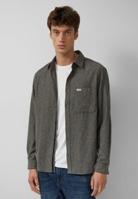 Grijze gestructureerde flanellen blouse met een button-down kraag, één borstzak en een contrasterend wit T-shirt eronder, gecombineerd met blauwe spijkerbroek.