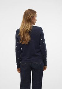 Navy sweater with white polka dots, featuring a round neckline and ribbed cuffs. Soft knit texture, casual fit, and simple design.