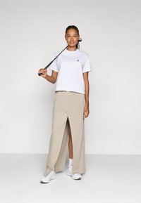 White cropped t-shirt and beige long skirt with a front slit, paired with white sneakers and holding a golf club, set against a neutral background.