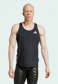 Muscular person with albinism wearing a black patterned Adidas tank top and black athletic leggings with wavy stripes, standing facing forward.