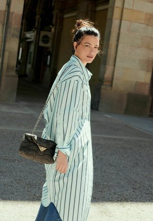 Lang blå og hvid stribet skjorte med en buet kant, parret med denim. Accessory: sort quilted håndtaske med kædestrop.
