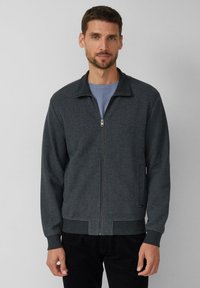 Dunkelgraue Jacke mit Reißverschluss, strukturiertem Muster, gerippten Bündchen und Saum, kombiniert mit einem hellblauen Rundhalsausschnitt-T-Shirt darunter.