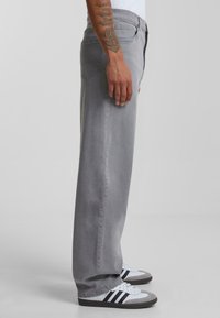 Gray denim jeans with a straight-leg design, five pockets, and subtle stitching details. Paired with white and gray sneakers.