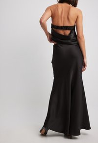 Abito da sera in satin nero con design senza spalline, schiena arricciata, silhouette fluida e drappeggio delicato per un aspetto elegante.