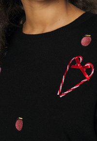 Svart stickad tröja med röd hjärt- och bärbroderi, med ett banddetalj på hjärtat och små guldförsköningar på bären.