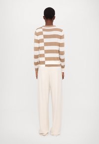Ribade beige ja valge kampsun, millel on mugav lõige, koos koorevärvi laiade pükstega. Pehme tekstuur, minimalistlik disain ja soonikkoes detailid mansettides.