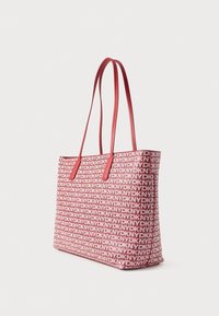 Punane kandekott, millel on korduv valge brändi logomuster, valmistatud vastupidavast tekstiivist, lamedate punaste nahkkäepidemete ja ristküliku kujuga.