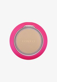 Rosa cirkulär behållare med ett klart lock, som avslöjar en beige produkt inuti. "FOREO"-logotyp prägla på ytan. Slät yta.
