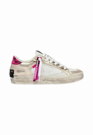 Sneaker bianca e oro con dettaglio rosa sul tallone, lacci bianchi e un'etichetta rosa con la scritta “Crime London” applicata sul lato.