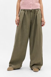 Pantalones de pierna ancha color caqui con un diseño plisado, cinturilla elástica y tela suave y texturizada; combinados con calzado estilo mocasín en color beige claro.