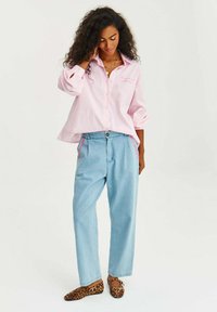 Ružovo-biely pruhovaný košeľový vrch s dlhými rukávmi v kombinácii so svetlomodrými nohavicami s vysokým pásom, ktoré majú ružové cik-cak švy, a leopardími balerínkami.