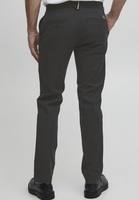 Vīriešu tumši pelēkas bikses, izgatavotas no kokvilnas sajaukuma. Tām ir taisna kāja, sānu un aizmugures kabatas ar pogu aizdari, kā arī discreti uzšuvumi.