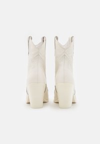 Białe skórzane kowbojki z ostrymi noskami, wypukłymi wzorami stębnowania i słupkowymi obcasami, o gładkiej teksturze i subtelnych metalicznych akcentach.