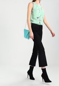 Blusa senza maniche verde chiaro con motivo floreale, abbinata a jeans neri alla caviglia e stivali neri. Borsa azzurra trapuntata con tracolla a catena.
