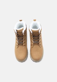 Brązowe wodoodporne buty z sztucznym futrem, sznurowany design, teksturowany język i gumowe podeszwy, z wyściełanym kołnierzem i pętlą z tyłu.