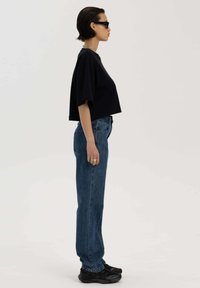 Zwarte cropped t-shirt met brede mouwen, gecombineerd met lichtgewassen straight-leg jeans en stevige zwarte sneakers. Eenvoudige zilveren ketting.