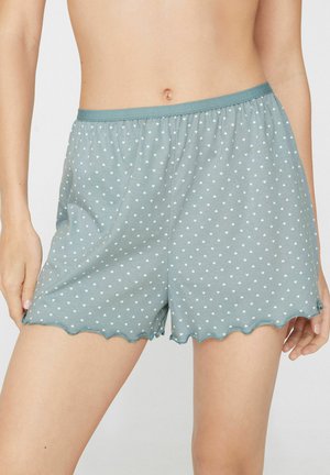 Hellblaue Shorts mit kleinen weißen Herzmustern und gewellten Rändern, getragen von einer Person, die von der Taille bis zur Mitte des Oberschenkels gezeigt wird.