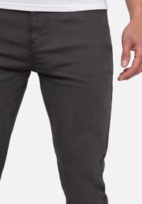 Tummanharmaat slim fit -housut, joissa on hienovarainen tekstuuri, ommellut yksityiskohdat ja keskikorkea vyötärö. Kangas näyttää kestävältä ja sileältä.