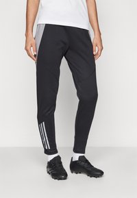 Black athletic pants with grey side panels, tapered design, and three white stripes on the left leg. Made of a smooth, stretchy material.