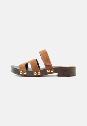Sandale mule en daim marron à bout ouvert avec un talon bloc en bois bas, deux brides horizontales et une bride de cheville ornée de clous dorés.
