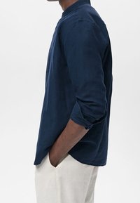 Laivaston sininen pitkähihaisen paita, jossa on vyöruusukaulus ja käännetyt hihansuut, valmistettu kevyestä kankaasta. Yhdistetty vaalean värisiin housuihin kontrastin aikaansaamiseksi.