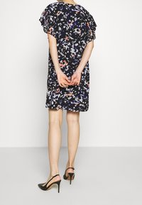 Robe florale avec un fond noir et des motifs multicolores, manches courtes froncées et coupe ample, associée à des talons aiguilles noirs.
