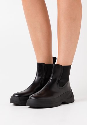 Black leather ankle boots with a chunky rubber sole, elastic side panels, and smooth finish, designed for easy wear and comfort.