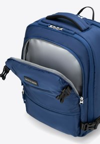 Modrá batoh z texturované tkaniny, s hlavním prostorem na zip a přední kapsou. Má polstrovanou rukojeť a odolné černé kovové akcenty.