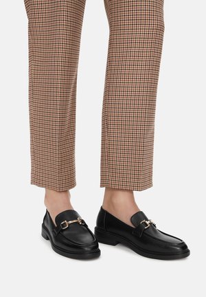 Czarne skórzane loafersy z metalicznym akcentem, okrągłym noskiem i krótkim blokowym obcasem, w zestawieniu z brązowymi spodniami w wzór houndstooth.
