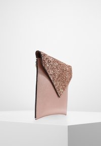 Vaaleanpunakultainen kirjekuorilaukku, jossa on teksturoitu keinonahkainen runko ja kimaltava glitterläppä, sekä tyylikkäät mustat reunat.