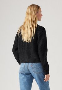 Μαύρος ριγέ πουλόβερ με στρογγυλή λαιμόκοψη και μακριά μανίκια, συνδυασμένο με αν�οιχτό μπλε ψηλόμεσα τζιν, προβάλλοντας άνετη εφαρμογή και υφασμάτινη υφή.