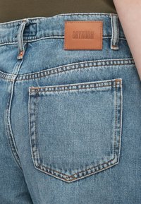 Lyseblå denimjeans med rett snitt, med oransje søm, en lapp med "DRYKORN" på baksiden, og en standard baklomme-design.